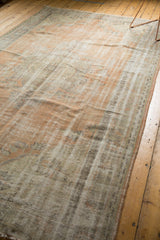 Distressed vintage Oushak carpet showcasing its open field, meandering border, and faded apricot and slate blue.