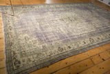 Distressed Oushak rug corner detail, showing purple, antique ivory, slate blue vinery, and fringe.
