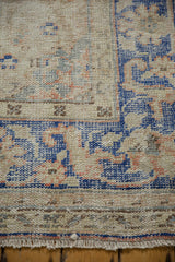 Textured distressed Oushak rug corner with faded cobalt blue border and fringe.