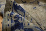 Folded vintage Oushak rug displaying distressed cobalt blue patterns on dusty ivory.