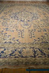 Distressed vintage Oushak rug close-up with pale apricot, cobalt blue floral vinery, and worn patterned border.