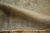 Curled edge of Distressed Oushak runner, showing textured pile, faint foundation, and fringe.