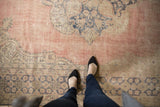 Distressed pile of vintage Turkish Oushak rug in pale blush, navy, and beige patterns.