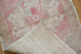 Distressed Oushak rug's folded corner displays even wear, pale pink pile, and hand-knotted back.