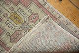 Distressed Oushak rug corner reveals worn dusty rose, gold pile, and hand-knotted foundation.