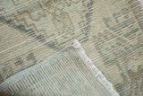 Distressed Oushak rug, highlighting muted beige pile, exposed hand-knotted foundation, and fringe.
