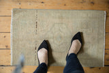 Distressed beige Oushak rug mat corner with even wear and pale seafoam motifs.