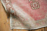 Distressed pink Oushak rug corner, showing fringe, aged texture, and striations.