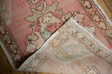 Folded corner of vintage Oushak rug, showing distressed pink pile and hand-knotted foundation.
