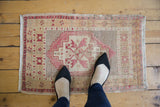 Distressed Oushak rug with pale red and ivory stepped medallion and geometric floral details.