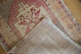 Vintage distressed Oushak rug folded, revealing geometric pale red pile and hand-knotted reverse.
