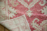 Faded cochineal red scrolling leaves on distressed Oushak rug pile, reverse and fringe.