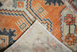 Distressed Oushak rug corner shows faded geometric pattern, pile wear, and visible hand-knotted foundation.