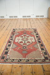 Distressed vintage Oushak rug corner: cherry red field, ivory lattice, charcoal border, white fringe.