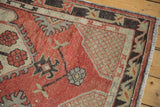 Distressed Oushak rug corner: cherry red field, ivory lattice spandrel, dark border, and fringe.