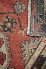 Close-up showing distressed cherry red Oushak rug pile, floral palmettes, and fringed foundation.