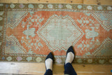 Distressed Oushak runner with faded rust and seafoam green delicate floral motifs.