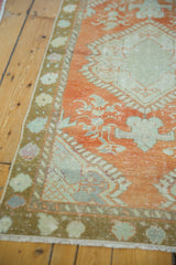Corner of distressed vintage Oushak runner, delicate pale rust and mint floral motifs, worn texture.