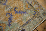 Corner of distressed Oushak rug runner, showing worn pile, dusty gold, seafoam green, and blue patterns.