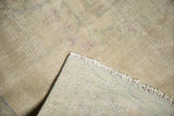 Corner of distressed Oushak rug showing pile wear, faint foundation, fringe, and hand-knotted reverse.