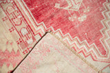 Distressed vintage Oushak rug corner revealing worn pale red, blush pile and ivory woven foundation.