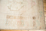 Pale ivory field and distressed low pile with soft pink, blue, bronze Oushak border motifs.