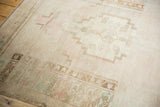 Distressed Oushak rug border showing pale pink, bronze, and powder blue motifs on ivory.