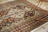 Angled close-up of geometric borders with orange animal motif on vintage Caucasian rug.