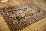 Vintage Caucasian rug with worn cherry red geometric border and tribal animal motifs.