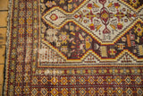 Worn vintage Caucasian rug corner, geometric diamond borders, stylized tribal motifs.