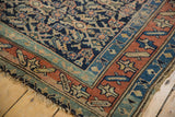 Antique Kurdish rug corner displaying madder red running border, Herati motif, and worn edges.