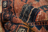 Folded detail of vintage West Persian rug, showing worn navy and brick red geometric motifs.