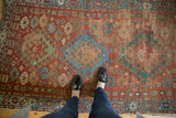 Antique Caucasian rug's triple medallion and geometric patterns with worn pile underfoot.