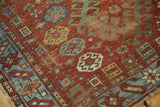 Antique Caucasian rug's red field, blue geometric border, with distinct pile wear and tattered selvage.