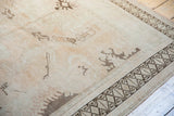 Distressed vintage Oushak carpet with worn beige field and dark geometric rams horn border.