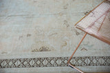 Close-up of a distressed Oushak rug with muted beige and dark rams horn border.