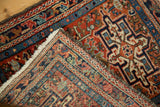 Folded vintage Karaja rug corner, showcasing geometric pinwheels in brick red and sky blue.