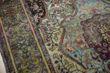 Detail of antique silk Kashan rug, showing rich aubergine, emerald, and gold curvilinear motifs.