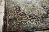 Antique silk Kashan rug corner revealing fine aubergine, green, and ivory floral patterns.