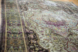 Lustrous silk pile with finely woven green, aubergine, and ivory floral motifs.