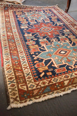 Fringed corner of an antique Heriz rug, showing geometric borders and worn pile with white knots.