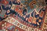 Folded antique Heriz rug shows navy, red geometric Karaja pattern and prominent pawn motif.