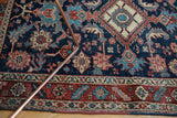Antique Heriz rug's lower section displaying dense floral vinery in navy, wine red, and ivory with subtle wear.