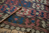 Hand woven antique Persian Kilim with madder root red and blue crab motifs, showing a tattered edge.