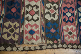 Antique Persian Kilim carpet's tattered edge and geometric madder red, blue, ivory patterns.