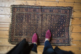 Antique Belouch rug corner detail: geometric trellis, starburst motifs, navy, brown, and frayed edges.