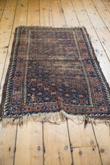 Antique Belouch rug with geometric patterns, navy, coffee brown, ivory tones, and tattered fringe.