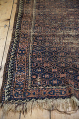 Antique Belouch rug's worn fringe and geometric wave border, navy and coffee brown.