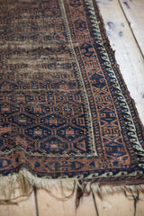 Close-up of the antique Belouch rug end, showing tattered fringe and geometric borders.