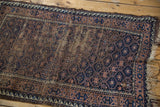 Corner of antique hand-knotted Persian Belouch rug with geometric navy, brown design and tattered ends.